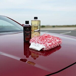 Premium Fahrzeug Pflege-Set mit Aktivschaum, Shampoo und feinem Waschhandschuh auf roter glänzender Motorhaube